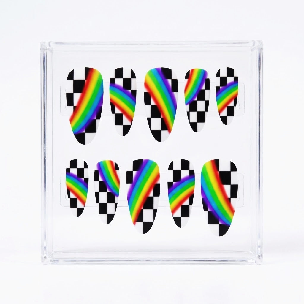 A clear acrylic nail display block containing ten almond press-on nails. Each nail features a black-and-white checkered pattern with a vibrant diagonal rainbow stripe running through the center.