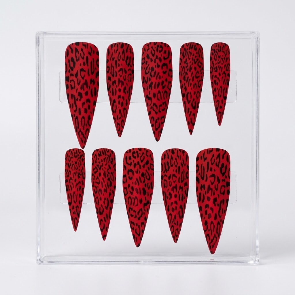 Ten red matte stiletto-shaped press-on nails with a black leopard print pattern, displayed inside a clear acrylic holder against a light gray background.