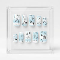 Ten square press-on nails arranged inside a clear acrylic display box on a white background. The nails have a light blue lined notebook paper pattern with various hand-drawn black doodles and symbols.