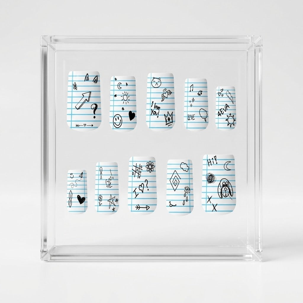 A set of matte square press on nails displayed inside a transparent square box, featuring a light blue lined notebook paper pattern with various black doodles and symbols.