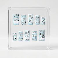 A set of matte square press on nails displayed inside a transparent square box, featuring a light blue lined notebook paper pattern with various black doodles and symbols.
