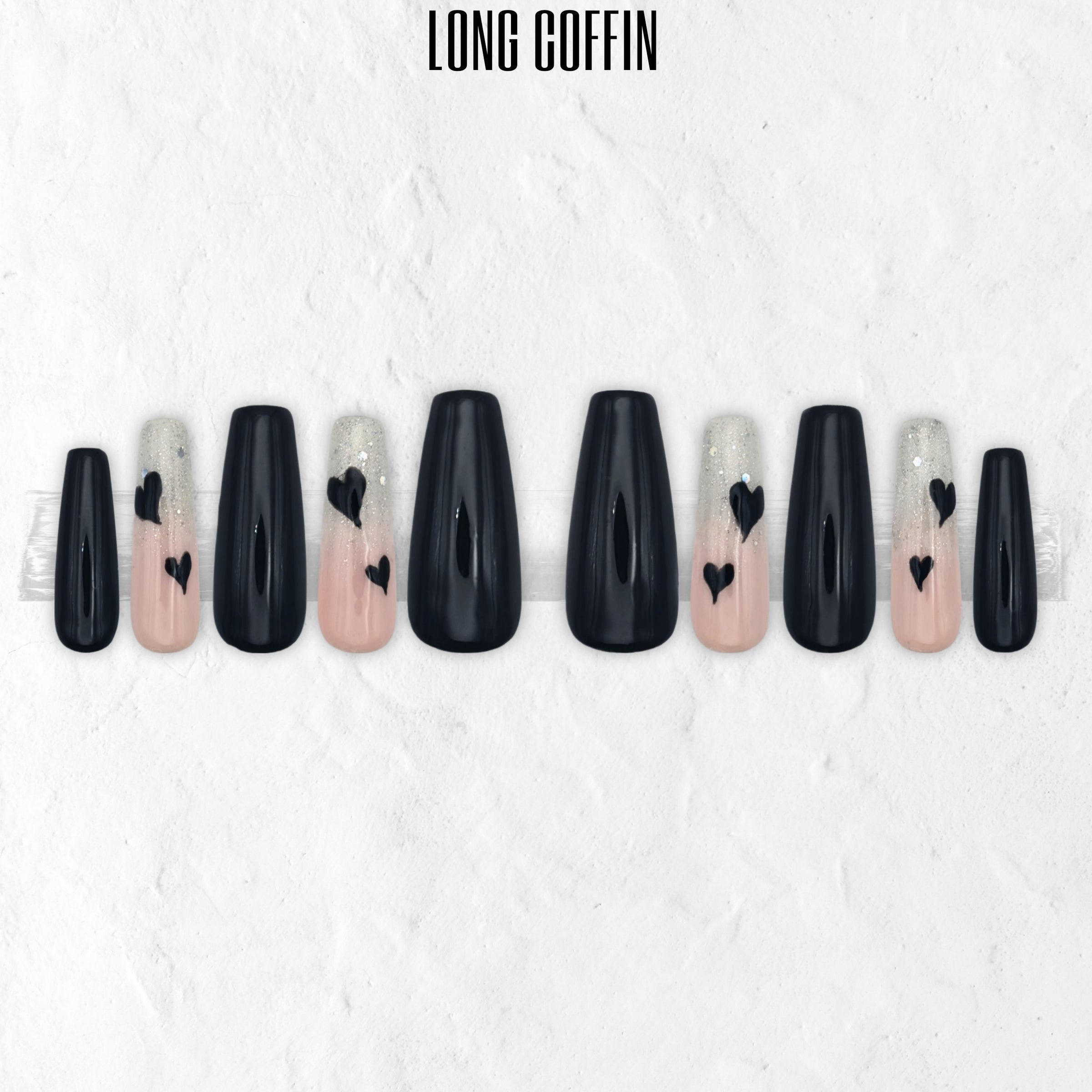 Glossy black and pink press-on nail set named Secret Admirer, featuring black nails, blush pink glitter ombré accent nails, and black heart nail art in a long coffin shape.
