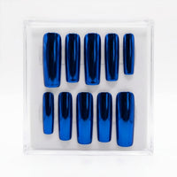 A set of ten metallic royal blue chrome press-on nails arranged in two rows inside a clear plastic display box on a white background.