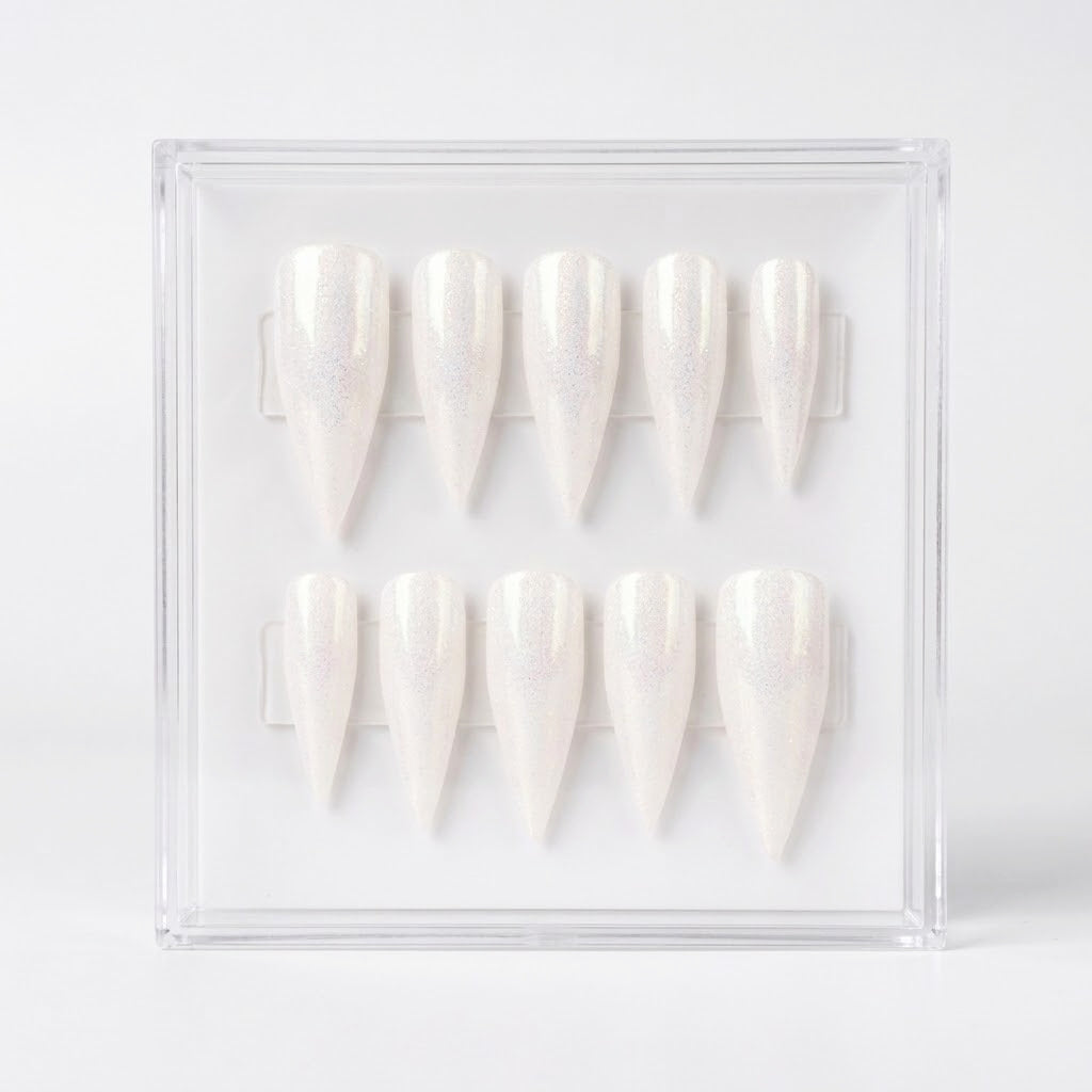 Ten stiletto-shaped press-on nails with a shimmering white finish, displayed inside a clear acrylic case on a light gray background.