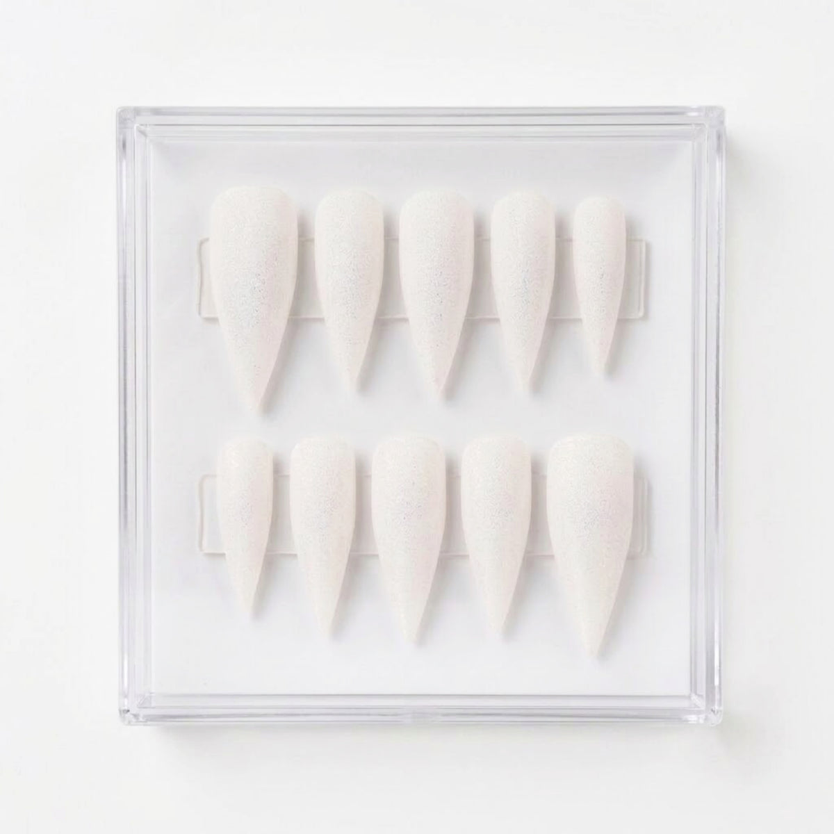 Ten shimmery matte white stiletto-shaped press-on nails arranged in two rows inside a clear plastic display case on a white background. 