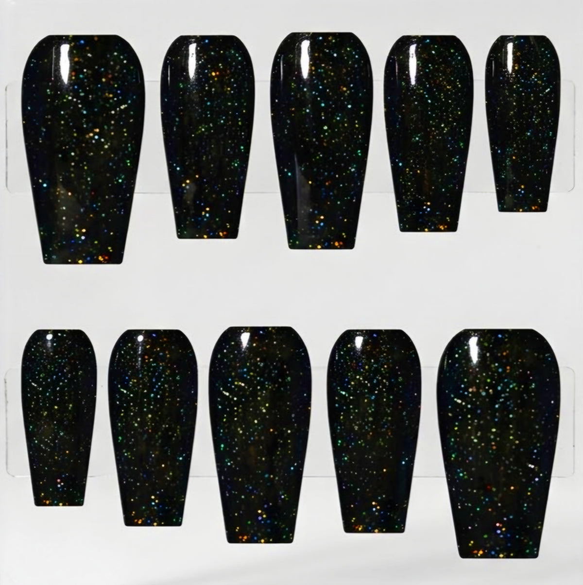 Ten coffin-shaped press-on nails with a glossy black base and dense multicolor iridescent glitter, arranged in two rows on a white background.