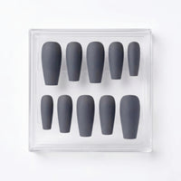 A set of ten matte dark gray press-on nails arranged in a clear plastic display box on a white background.