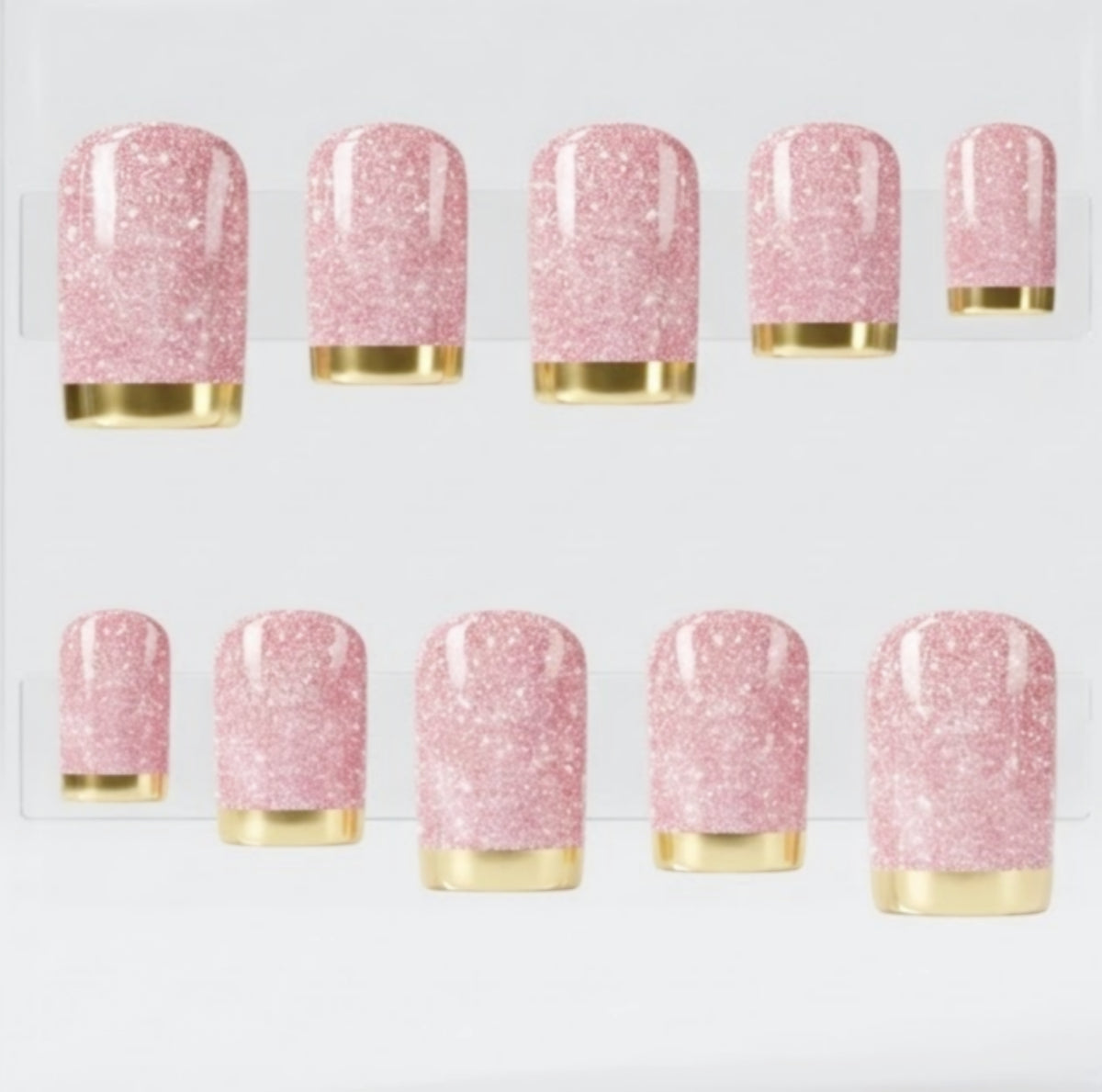 A clear acrylic block displaying 10 square pink glittery press on nails with chrome gold tips, arranged in two rows on a white background.
