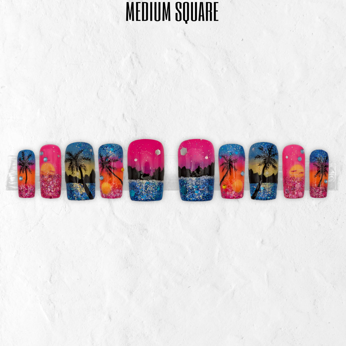 Sunset Lagoon tropical press-on nails with pink, orange and blue sunset nail art, palm tree silhouettes, glitter details and glossy medium square false nails.