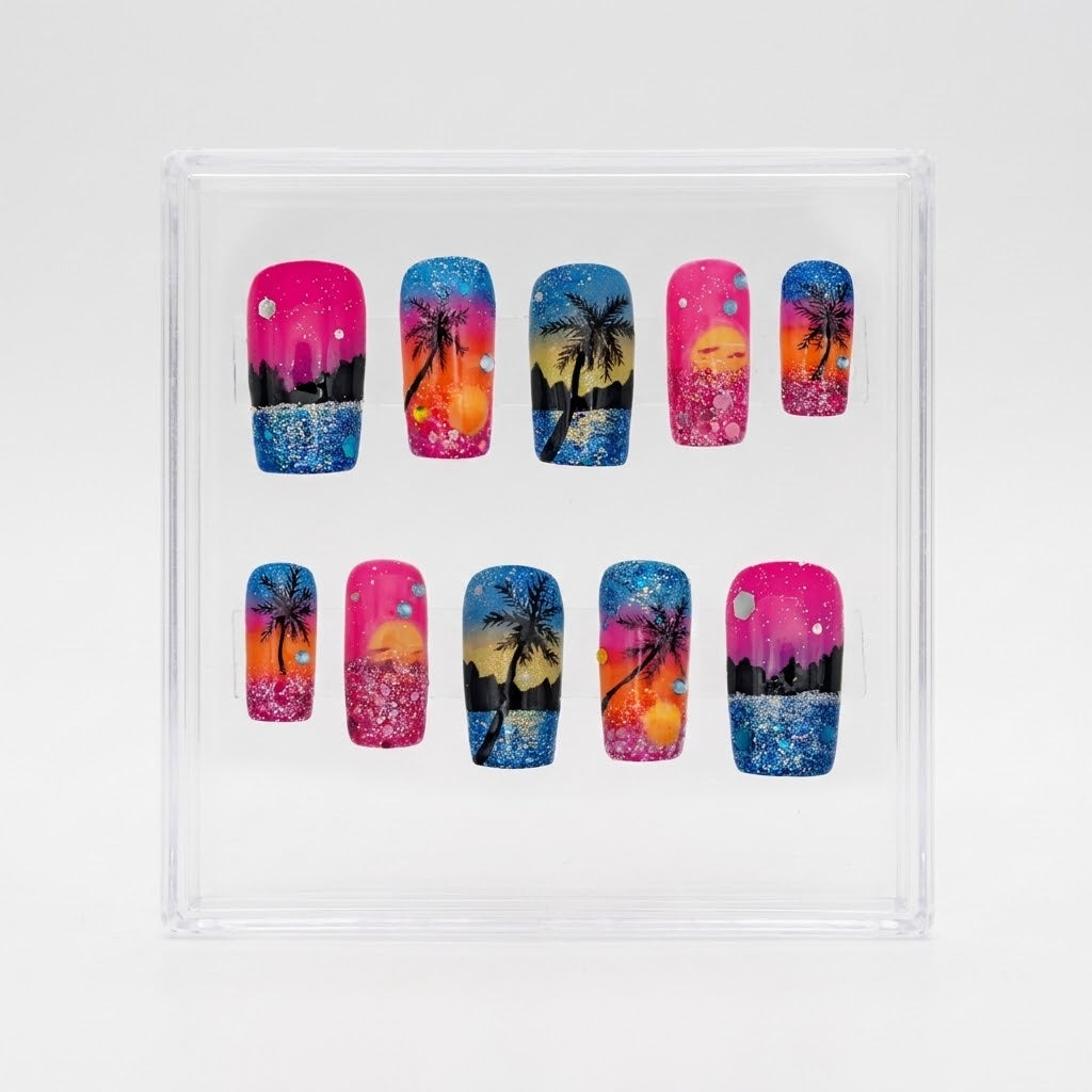 A set of 10 square press-on nails displayed inside a clear plastic square box on a light gray background. The nails feature vibrant tropical beach scenes with pink, orange, yellow, and blue sunset gradients, black palm tree silhouettes, and glittery blue water details.