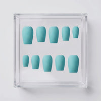 A set of ten press-on nails in a soft mint blue color, arranged inside a clear acrylic display box on a light gray background.