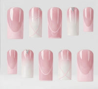 Ten square pink and white gradient false nails with heart and swirl designs with rhinestone details, arranged in two rows on a light gray background.