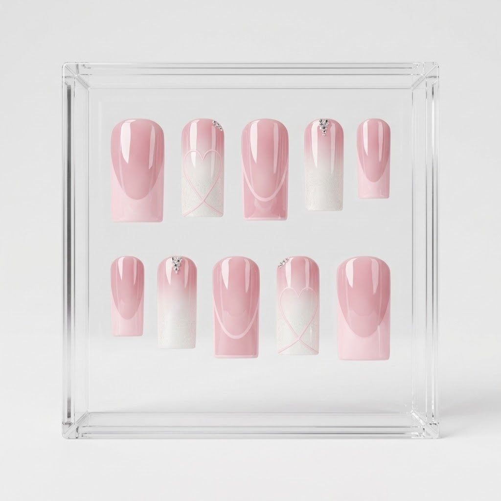 A set of 10 square press-on nails displayed inside a clear acrylic square box on a light gray background. The nails feature a pink and white ombre gradient design with delicate white line art and small rhinestone accents.