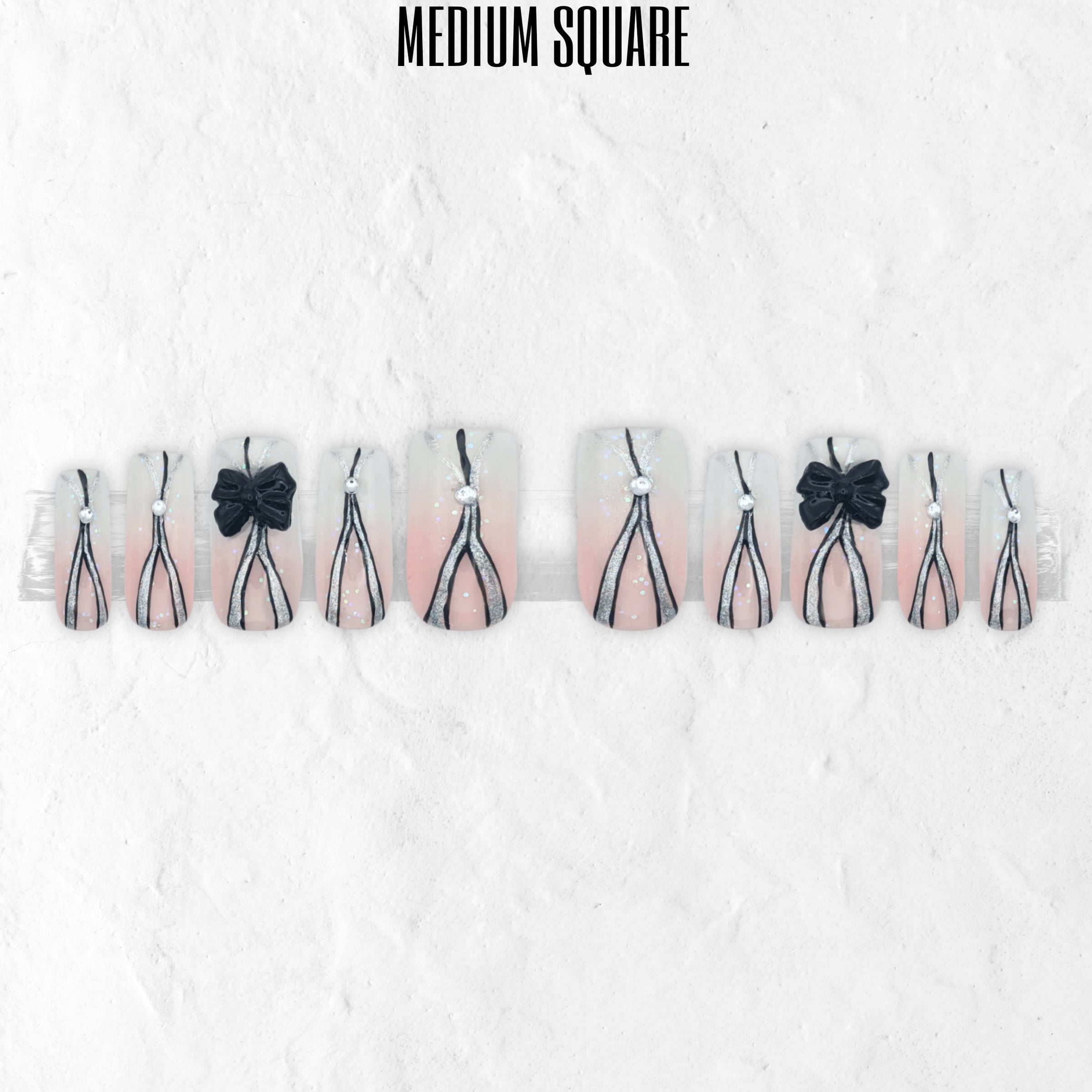 Tie Me Pretty pink and black press-on nails with corset lace-up nail art, bow accents and glossy medium square false nails.