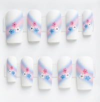 A set of 10 square white glossy press on nails featuring a trans colours themed design. With pink and pale bue ombre swipe and small pink, blue and white flowers with rhinestone centres.
