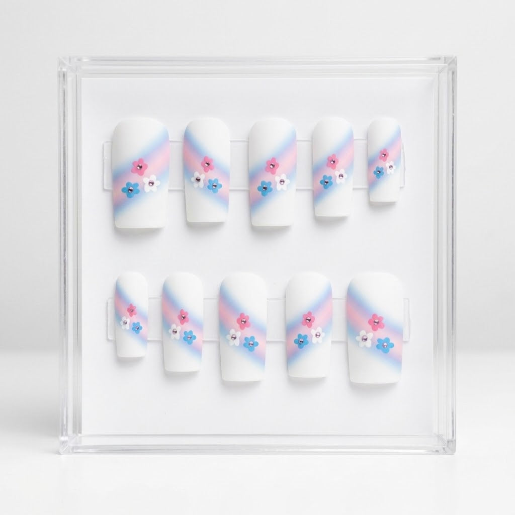 A set of 10 square white glossy press on nails featuring a trans colours themed design. With pink and pale bue ombre swipe and small pink, blue and white flowers with rhinestone centres.