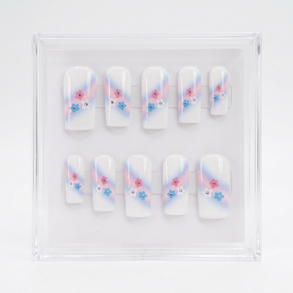 A set of 10 square white glossy press on nails featuring a trans colours themed design. With pink and pale bue ombre swipe and small pink, blue and white flowers with rhinestone centres.