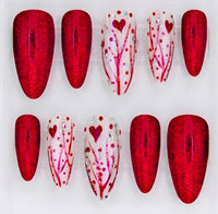 A set of 10 almond  press-on nails displayed in a clear acrylic case on a white background. The set features alternating red glitter and white decorated with red hearts and branch patterns.