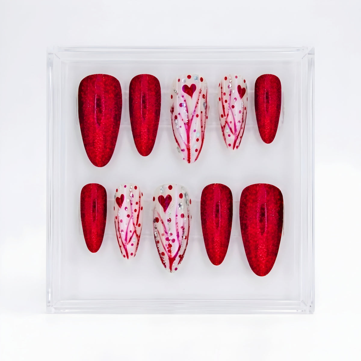 A set of 10 almond  press-on nails displayed in a clear acrylic case on a white background. The set features alternating red glitter and white decorated with red hearts and branch patterns.