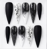 Ten black and white stiletto-shaped press-on nails arranged in two rows on a white background, featuring solid matte black, glossy black glitter gradient, and white with black scrollwork designs.