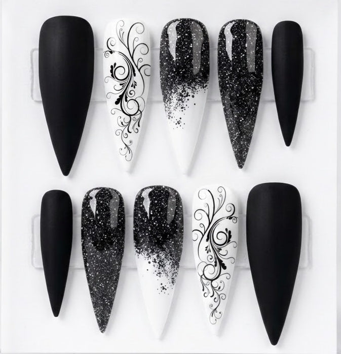 Ten black and white stiletto-shaped press-on nails arranged in two rows on a white background, featuring solid matte black, glossy black glitter gradient, and white with black scrollwork designs.