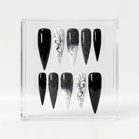 A set of 10 black and white Stiletto-shaped press-on nails displayed in a clear acrylic case against a light gray background.