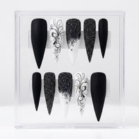 A set of 10 black and white stiletto-shaped press-on nails displayed inside a clear plastic storage box against a white background.