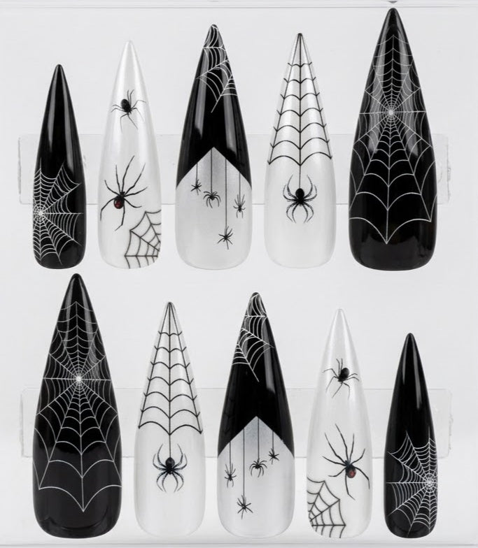 Ten pointed false nails displayed on clear plastic hangers, featuring black and white spiderweb and spider designs.
