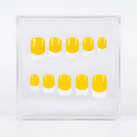 A set of ten press-on nails with a yellow and white French tip design, displayed inside a clear acrylic case on a white background.